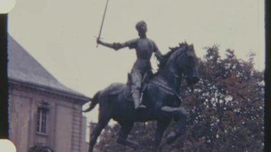 Jeanne d 'Arc' ın at sırtındaki bir heykeli, 8mm 'lik bir filme alındı, arka planda ağaçlar ve binalar olan bir açık hava ortamında göze çarpıyor..
