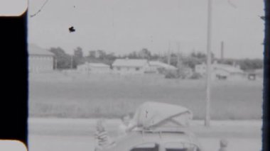 8 mm 'lik bir görüntü, bir baba ve çocuklarının birlikte çalışıp çantalarını ve teçhizatlarını arabaya yükleyip ilerideki eğlenceli bir yolculuğa hazırlandıklarını gösteriyor.