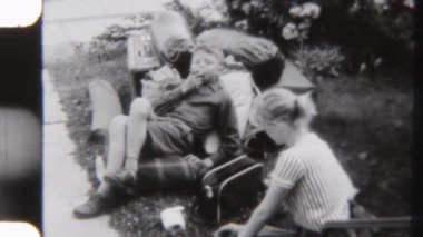 8 mm 'lik bir video, kız kardeşi bahçedeki çimlerin üzerinde eşyalar düzenlerken ve bir yaz macerasına hazırlanırken paketlenmiş çantalara yaslanan bir çocuğun görüntüsü.