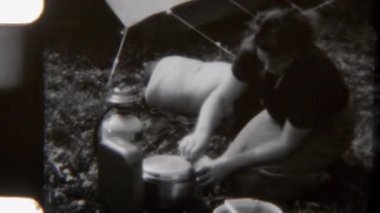 8 mm 'lik bir anne çadırın yanında dikkatlice bir tencereyi açarken çekilmiş görüntüler. Yemeğin kırsal bir kamp gezisinde pişirilip pişirilmediğini kontrol ediyor.