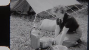 Bir annenin kırsal bir kamp gezisi sırasında çadırın yanında kamp yemeği hazırlarken çekilmiş 8mm 'lik eski bir görüntü.