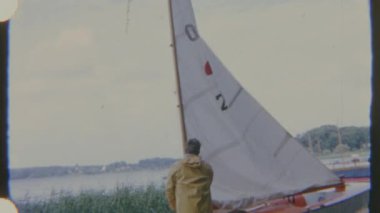 Sarı yağmurluklu bir adam, bir yelkenlinin yanında duruyor. Su birikintisinin yanında, 8 mm 'lik bir filmde yakalandı. Sahne sakin ve huzurlu bir ruh hali veriyor..