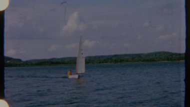 Bir adam sakin sularda küçük bir yelkenliyi yüzdürüyor, sakin ve huzurlu bir görsel havayla 8 mm 'lik bir filme çekiliyor. Yelkenlinin hareketi suda süzülürken pürüzsüz ve sabittir.