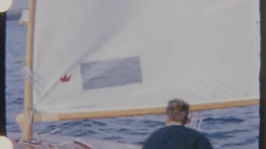 Bir adam mavi sularda eski bir tekne kullanıyor, 8mm 'lik bir filme çekiliyor maceracı ve nostaljik bir ruh hali içinde..