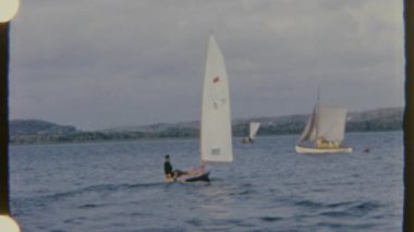 Bir adam ufukta manzarası görünen dalgalı sularda küçük bir tekneyi kontrol etmeye çalışıyor. 8mm 'lik bir filme çekilen sahne nostaljik bir atmosfer taşır..
