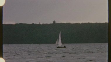 İki yelkenli sakin sularda süzülüyor, temiz bir gökyüzünün altında uzak bir kıyı manzarasıyla 8 mm 'lik bir filme çekiliyor..