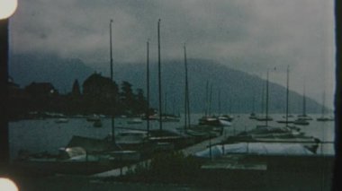 8mm 'lik Retro film, bir rıhtıma yanaşmış sayısız yelkenlinin bulunduğu sakin bir göl manzarasını yakalıyor. Sakin su bulutlu gökyüzünü yansıtır, sakin ve nostaljik bir atmosfer yaratır..