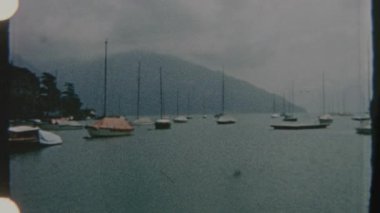 8mm 'lik Retro film, sakin bir göl manzarası yakalıyor. Yelkenliler yavaşça suda sürükleniyor. Bulutlu gökyüzü yumuşak bir ışık yayar, dingin ve nostaljik bir atmosfer yaratır..