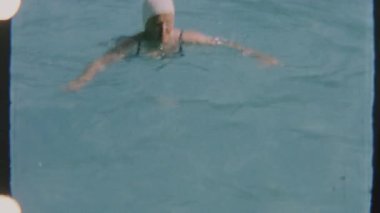 Otantik 8 mm film, berrak havuz sularında yüzme şapkasıyla süzülen bir kadının nostaljik bir yaz havasını anımsattığı huzurlu bir anı yakalıyor..