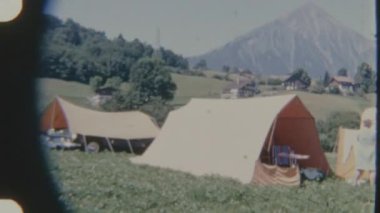 Çimenli bir arazide çadır kamp alanı. Dağ zemininde, 8 mm 'lik bir filme çekilmiş. Huzurlu ve manzaralı bir görsel ortam yaratıyor..