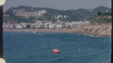 8mm filmle çekilen sakin bir kıyı kasabası manzarası, yumuşak dalgalar ve ağaçlarla dolu küçük bir ada, sakin ve görsellik dolu bir ortam yaratıyor..