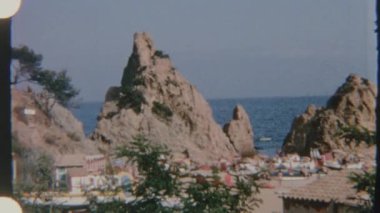 Sahile yakın kayalık oluşumlar ve kayıklarla dolu bir plaj sahnesi, gündüz vakti çekilen 8 mm 'lik bir filmle çekildi..