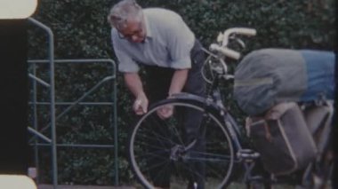 Yaşlı bir adam kaldırımda torba dolu bir bisikleti tamir ediyor. Gündüz vakti çekilen 8 mm 'lik filmle..