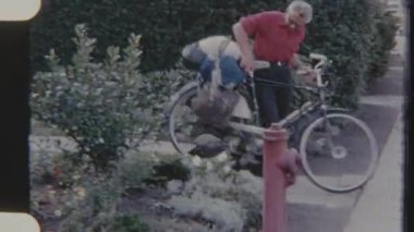 Yolculuk için paketlenmiş bisikletleriyle yola çıkan bir çiftin 8mm 'lik klasik filmi. Sokakta park etmiş bir Volkswagen Beetle' ı var..