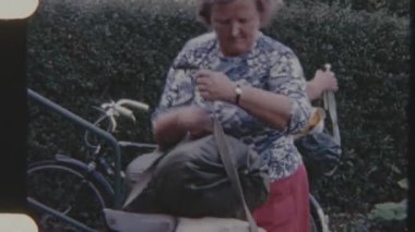 8 mm 'lik bir çift bisikleti sürmeden önce paketliyor ve ayarlıyor. Bisiklet yolculuğuna hazırlanırken kadın bavulları emniyete alıyor..