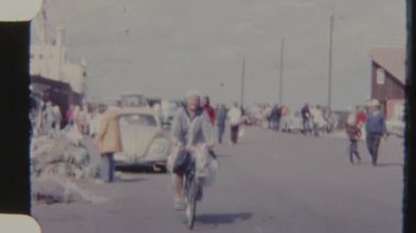 Orta yaşlı bir kadın hareketli bir cadde boyunca bisiklet sürüyor ve 8 mm 'lik bir filme çekiliyor. Sahne, feribot terminalinin yanındaki yolda yayalar ve park etmiş arabalarla dolu..