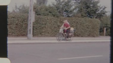 İki bisikletçi, bir erkek ve bir kadın, 8 mm 'lik kamerayla çekilen, bisikletlerine bağlı bir bavulla kaldırımda yan yana gidiyorlar. Sahne, seyahat ve hareket duygusunu doğal bir ortamda iletir..