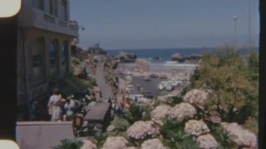 Sahilde kalabalık bir cadde, merdivenlerden inip çıkan insanlar ve park halindeki arabalarla dolu bir kaldırım boyunca, gündüz vakti çekilen 8 mm 'lik bir film..