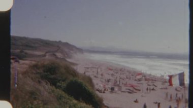 Kalabalık bir plajın panoramik 8 mm 'lik filmi. Gündüz güneşlenen ve yüzen insanlar..