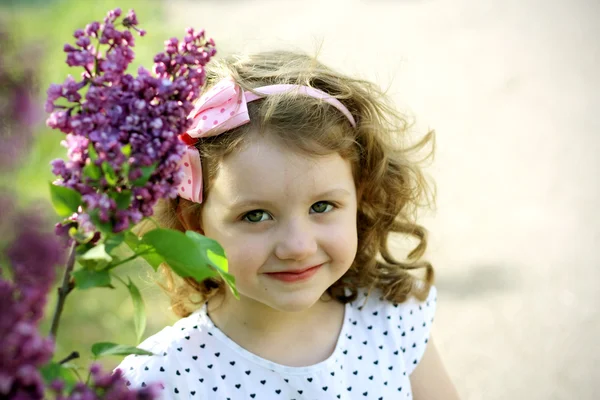 Lilla lockiga flicka nära blommande Syren — Stockfoto