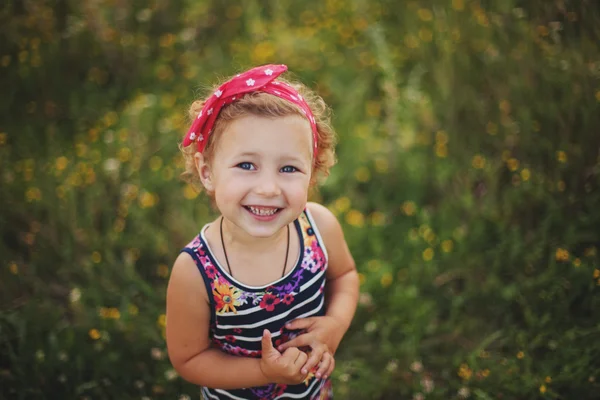 Lächelndes kleines Mädchen in buntem Kleid auf dem Sommerfeld — Stockfoto