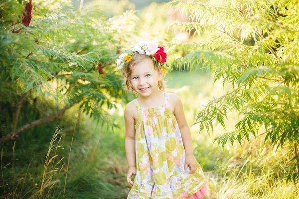 Kleines Mädchen im Blumenkranz im Garten — Stockfoto