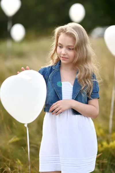 Ritratto di una bambina in un campo con palloncini bianchi — Foto Stock