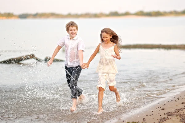 Портрет мальчика и девочки, бегущей по пляжу — стоковое фото
