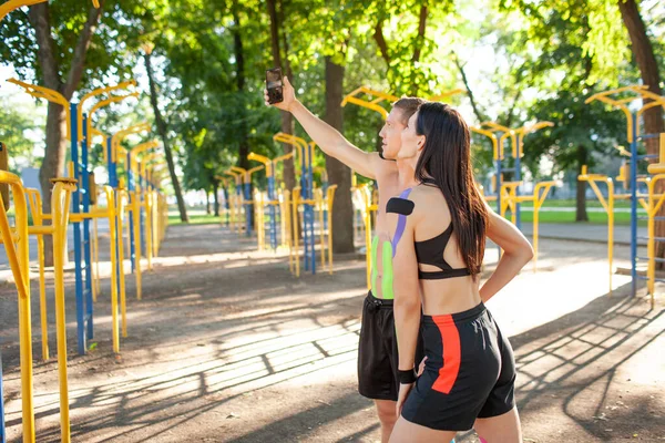 Pareja deportiva con cinta kinesiológica tomando selfie al aire libre. — Foto de Stock