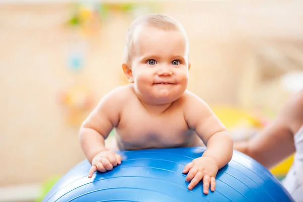 Lachende baby liggend op grote blauwe fitness bal thuis. — Stockfoto