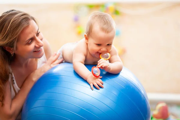 Bambino che tiene giocattolo sulla palla da ginnastica con la madre. — Foto Stock