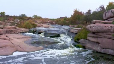Pürüzsüz ve karanlık taşların arasında küçük parlak bir dere akıyor.