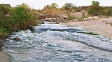 Pürüzsüz ve karanlık taşların arasında küçük parlak bir dere akıyor.