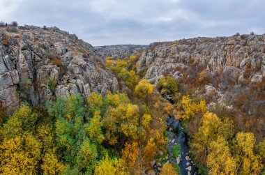 Aktovsky Kanyonu, Ukrayna 'da bir dere akar. Etrafta sonbahar ağaçları ve büyük taş kayalar var. Hava panoramik İHA görüntüsü