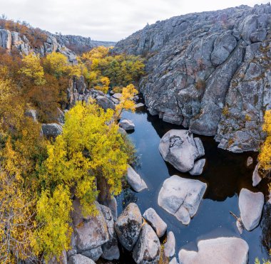 Aktovsky Kanyonu, Ukrayna 'da bir dere akar. Etrafta sonbahar ağaçları ve büyük taş kayalar var. Hava panoramik İHA görüntüsü