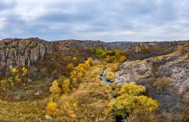Aktovsky Kanyonu, Ukrayna 'da bir dere akar. Etrafta sonbahar ağaçları ve büyük taş kayalar var. Hava panoramik İHA görüntüsü