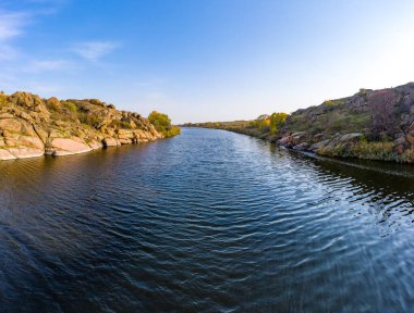 Ukrayna 'daki sıcak akşam ışığında küçük kuru bitkilerle kaplı büyük taşların arasında akan bir dere. Hava aracı görüntüsü