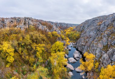 Aktovsky Kanyonu, Ukrayna 'da bir dere akar. Etrafta sonbahar ağaçları ve büyük taş kayalar var. Hava panoramik İHA görüntüsü