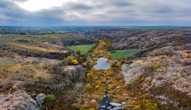 Aktovsky Kanyonu, Ukrayna 'da bir dere akar. Etrafta sonbahar ağaçları ve büyük taş kayalar var. Hava panoramik İHA görüntüsü