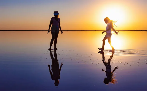 Deux charmantes sœurs marchent le long du lac miroir dans le coucher de soleil ardent du soir — Photo