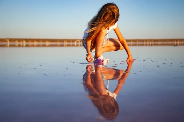 Una niña hermosa está mirando algo en una superficie de agua transparente sobre un fondo transparente —  Fotos de Stock