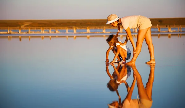 Two fantastically beautiful girls on a beautiful transparent lake are looking for something in a shiny surface — Stock Photo, Image