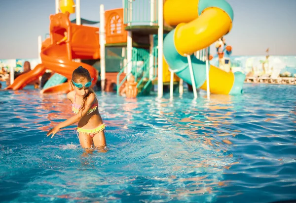 Una chica alegre con gafas azules para nadar gira en una piscina con agua clara y clara con las manos en el agua — Foto de Stock