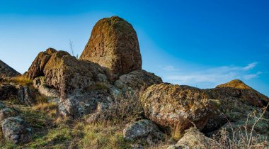 Ukrayna 'nın sıcacık güneşi ve güzel doğası ile dolu bir çayırda bitki örtüsüyle kaplı eski taş minerallerinin devasa birikintileri.