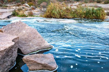 Pürüzsüz, ıslak ve karanlık taşların ve kuru alçak ağaçların arasında küçük, parlak bir dere akıyor.