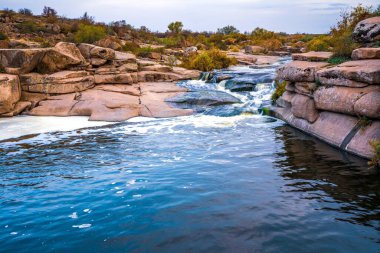 Pürüzsüz, ıslak ve karanlık taşların ve kuru alçak ağaçların arasında küçük, parlak bir dere akıyor.