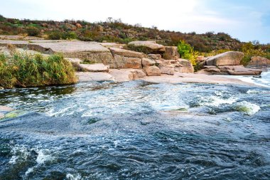 Pürüzsüz, ıslak ve karanlık taşların ve kuru alçak ağaçların arasında küçük, parlak bir dere akıyor.