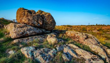 Büyük yeşil-sarı bir tarlada küçük bir taş yığını olağanüstü güzel mavi bir gökyüzünün arka planına karşı.