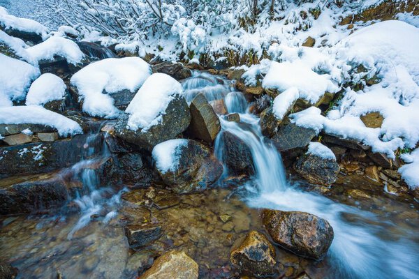 Small fast stream among small wet stones and cold white snow in the picturesque Carpathian mountains in beautiful Ukraine and its fantastic nature