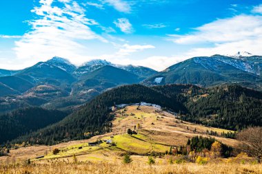 Karpat dağlarını kaplayan güzel renkli ormanlar ve sıcak sonbahar gökyüzünün arka planında küçük bir köy.
